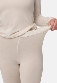 Beżowa, lekka, termiczna bluzka bazowa z długimi rękawami, połączona z dopasowanymi legginsami. Miękka faktura, subtelne szwy, elastyczny pas.