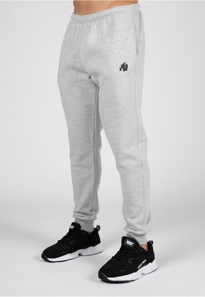 Grijze sweatpants van zacht materiaal met een slim fit en een geborduurd zwart gorilla-logo. Gecombineerd met zwarte sportschoenen.