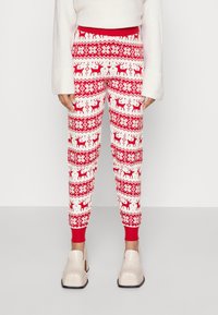 Czerwono-białe spodnie dresowe w wzory z motywami reniferów, geometrycznymi desenami oraz ściągaczem w talii; wykonane z miękkiego, teksturowanego materiału.