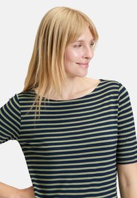 Koszula w paski w kolorze granatowym i oliwkowym, z dekoltem w łódź i krótkimi rękawami, wykonana z miękkiego, lekkiego materiału. Dopasowany krój, gładka tekstura.