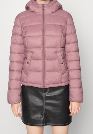 Mujer con chaqueta acolchada con capucha en tono rosa polvoriento, con cremallera frontal y bolsillos con botones, combinada con una minifalda de cuero negra.