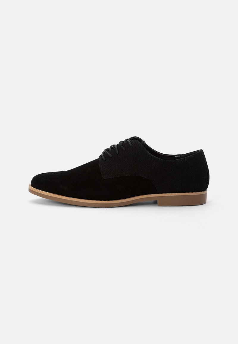 Chaussure habillée à lacets pour homme en suède noir et tissu avec semelle couleur noisette, vue de profil sur fond blanc.