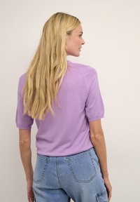 Top in magenta a maniche corte, con una vestibilità rilassata, texture morbida e polsini a coste. Indossato con pantaloni di jeans azzurri a vita alta.