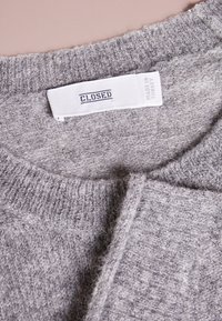 Grau gestrickter Pullover mit geripptem Kragen und Saum, weicher Textur, mit einem Etikett, auf dem "CLOSED" und "MADE IN TURKEY" steht.
