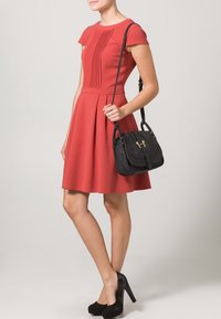 Röd kortärmad klänning med plisserad överdel, utsvängd kjol och midjeband. I sällskap med en svart axelväska med guldaccenter.