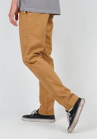 Pantalons chino de couleur beige, coupe slim, dotés de poches avant, associés à des baskets noires avec des semelles et des lacets blancs.