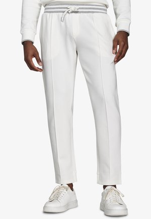 Męskie białe spodnie dresowe w fasonie slim-fit z elastycznym paskiem w szare paski i białe trampki, krótkie ponad kostkami.