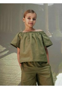 Blusa verde oliva con scollo off-the-shoulder, collo arricciato e maniche corte, abbinata a pantaloni verde oliva coordinati, realizzati in tessuto morbido.