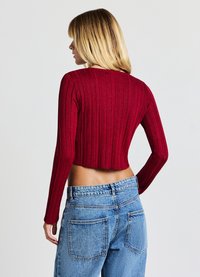Roter, gerippter Kurzpullover mit langen Ärmeln, kombiniert mit hellblauen, hoch taillierten Jeans mit großen Gesäßtaschen. Glatte Textur und enganliegendes Design.