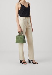 Černý saténový top na ramínka, krémové džíny s vysokým pasem, zelená strukturovaná kabelka s dvojitými uchy, a černé sandály na podpatku s pásky.