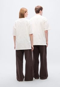 Κρεμ oversized t-shirts με ανάγλυφο σχέδιο, συνδυασμένα με φαρδιά καφέ παντελόνια. Τα υφάσματα φαίνονται μαλακά και υφασμένα.