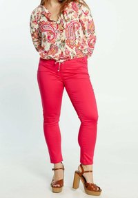 Floral blouse with pink paisley patterns, tied at the waist, paired with bright pink skinny jeans and brown block-heeled sandals.