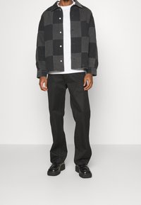 Schwarz-grau kariertes Jeansjacke, getragen über einem weißen T-Shirt. Kombiniert mit schwarzen Hosen und klobigen schwarzen Schuhen.