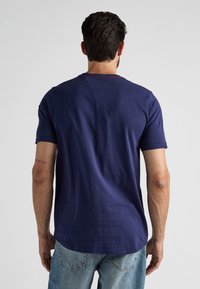 Granatowa koszulka z krótkim rękawem z okrągłym dekoltem i delikatnym wykończeniem. Miękka tkanina o gładkiej fakturze, z kontrastowym czerwonym akcentem przy kołnierzyku.