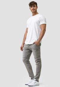 Camiseta blanca de algodón, jeans ajustados de mezclilla gris con detalles de costura, combinados con zapatillas blancas. Conjunto casual, colores neutros, diseño moderno.