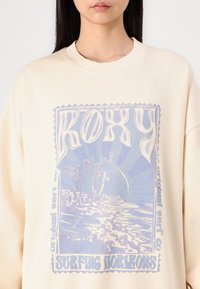Kremfarget sweatshirt med grafisk trykk som viser palmer, bølger og teksten "Roxy Surfing Horizons" i blå og lilla toner.
