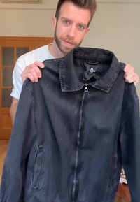 Černá džínsová bunda s límečkem, zipem vpředu a dvěma bočními kapsami. Materiál má strukturovaný povrch a volný střih.