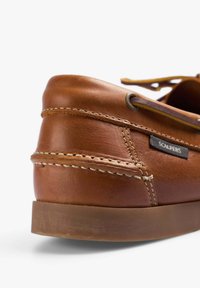 Bruine leren boot-schoen met contrasterende stiksels, rubberen zool en een merketiket aan de zijkant. Veters door metalen oogjes geregen.