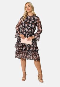 Svart blommig klänning med långa, volangiga ärmar och lager av volang framtill. Har ett genomskinligt överdrag med rosa och vita blommönster.