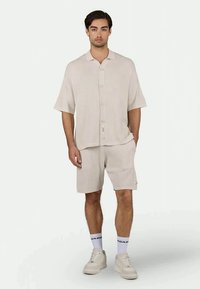 Camisa de botão de manga curta em tom bege claro com nervuras, combinada com calções iguais. Ajuste casual com uma superfície texturada e etiqueta de logotipo nos calções.