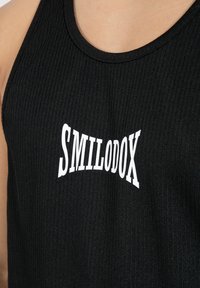 Schwarzes ärmelloses Tanktop aus geripptem Stoff, mit einem weißen Grafiklogo "SMILODOX" in der Mitte. Glatte Textur und runder Ausschnitt.