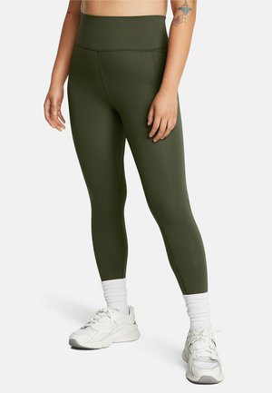 Høj taljede olivengrønne leggings lavet af strækbart materiale, med et sømløst design og en glat tekstur, båret med hvide sneakers og sokker.