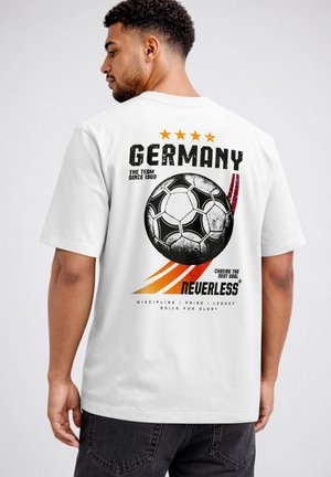 Man wearing white t-shirt with Germany soccer ball graphic, four stars, and text about pride and legacy on the back.
