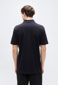 Μπλε ναυτικό πόλο μπλουζάκι με υφή υφάσματος, μαλακό γιακά και μανίκια που είναι γυρισμένα. Διαθέτει άνετη εφαρμογή, με ίσια γραμμή στο πίσω μέρος.