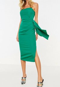 Grön, ärmlös midikjol med en figurnära silhuett, draperad sidodetailj och hög sprund. Tillverkad av ett mjukt tyg med en lätt lyster.