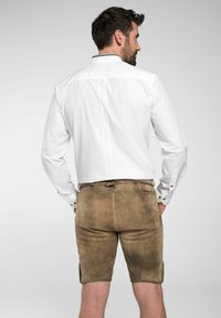 Weißes Langarmhemd mit geknöpften Manschetten, kombiniert mit braunen Wildleder-Shorts mit Seitentaschen und einem Bund mit Kordelzug.