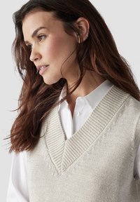 Hellgraue Strickweste mit V-Ausschnitt und gerippten Kanten, über ein weißes Hemd mit Kragen gelegt. Weiche Textur mit einem lässigen Design.