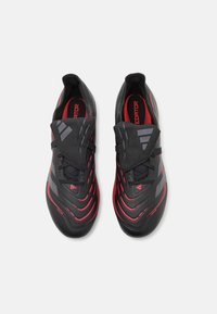 Black and red soccer shoes with a textured upper, streamlined shape, striking red lines, and integrated laces. Accented with gray details.