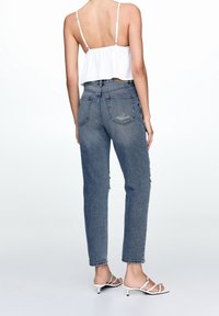 Ljusblå högmidjade jeans med avslappnad passform, med en blekt textur och subtil slitage. Kombinerat med en vit kort topp och sandaler.