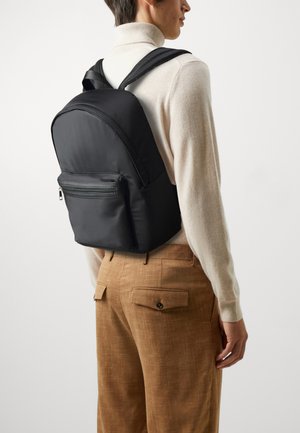 Black nylon backpack with a rounded top, front zip pocket, and adjustable straps. Smooth texture with subtle stitching details.