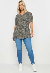 Top corto de manga corta en blanco y negro con un diseño de estampado, con escote en V, combinado con jeans ajustados azules y zapatillas blancas. Estilo casual, ajuste relajado.