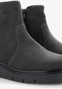 Harmaat mokkasiini nilkkurit, joissa on virtaviivainen muotoilu, sivuvetoketju ja teksturoitu musta alusta, jossa on selkeät urat.