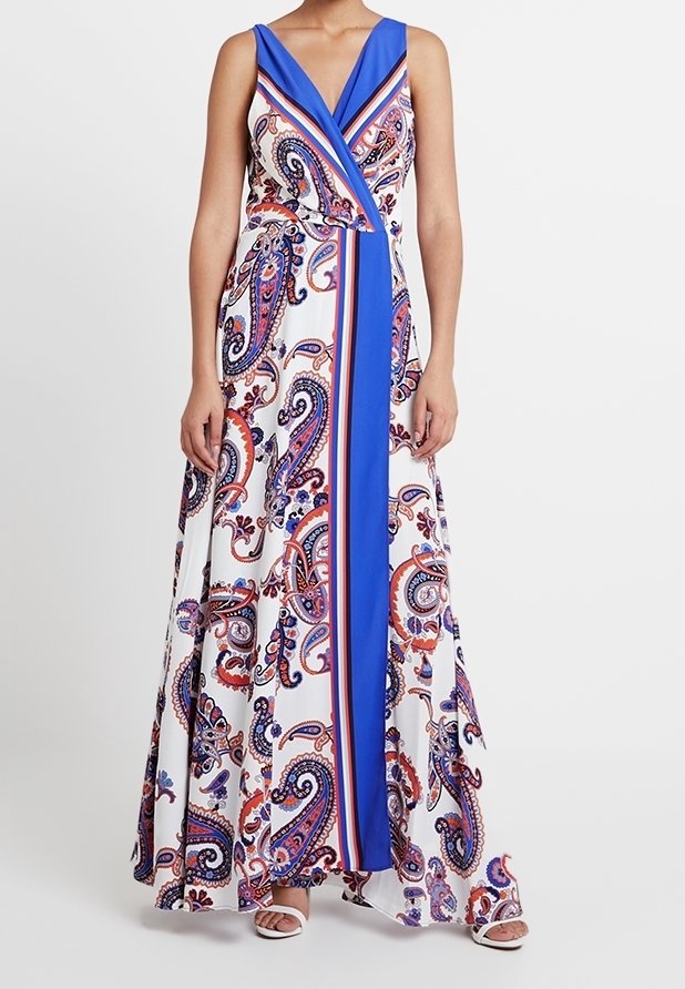 Robe maxi sans manches avec motif cachemire bleu, blanc et rouge et un panneau vertical bleu uni, portée avec des sandales blanches ouvertes.