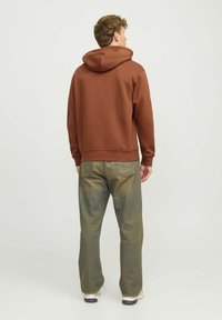 Brown hoodie with a hood, ribbed cuffs, and waistband. Worn with light green jeans and beige sneakers. Simple, casual design.