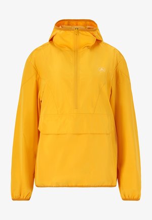 Manos sosteniendo y desplegando una chaqueta impermeable amarilla brillante y su bolsa de almacenamiento a juego, llevada por una persona con ropa beige.
