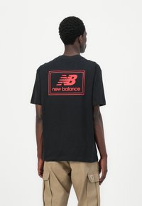 T-shirt en coton noir arborant un logo "New Balance" rouge au dos, avec des manches courtes et une coupe décontractée.