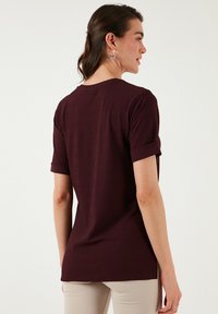 Burgundi värvi ribadega topp lühikeste keeratud varrukatega, ümmarguse kaelusega ja veidi kumerate servadega. Sile, veniv kangas, mis rõhutab figuuri.