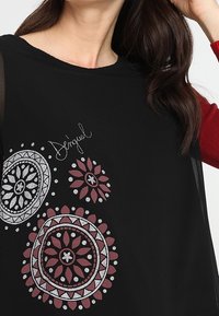 Tunic nera con motivi mandala rossi e argento. Tessuto morbido con una vestibilità comoda e design minimalista, scollatura rotonda e maniche trasparenti.