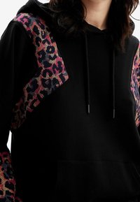 Sweat à capuche noir avec des accents d'imprimé léopard coloré sur les épaules, doté d'une capuche avec cordon de serrage, d'une poche avant et d'un tissu doux au toucher.