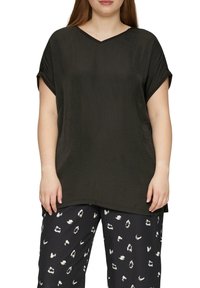 Schwarzes kurzärmliges Oberteil mit einem V-Ausschnitt und strukturiertem Stoff, kombiniert mit gemusterten schwarz-weißen Hosen mit einem Tierdruck.