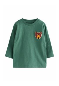 Chemise verte à manches longues en tissu doux, ornée d'un patch en forme de tête d'ours sur la poitrine gauche. Design simple avec un col rond et une coupe décontractée.