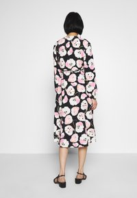 Svart klänning med ett blommönster som har stora vita och rosa blommor, långa ärmar och cinchad midja, som är matchad med svarta sandaler.