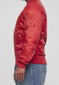 Giacca bomber rossa in tessuto satinato, con polsini e orlo a costine, tasca con zip sulla manica sinistra, tasche laterali e una silhouette aderente.