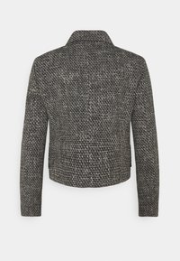 Chaqueta de tweed en blanco y negro con un cuello estructurado, mangas largas y diseño corto, que presenta un acabado tejido texturizado.