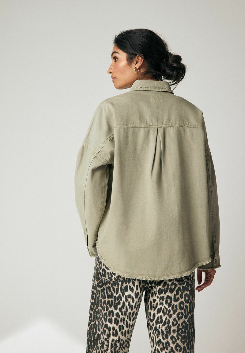 Šviesiai žalia didelio dydžio marškinėliai su išlenktu kraštu, su nugaros raukšle, derinami su juodais ir smėlio spalvos gyvūnų rašto kelnėmis.