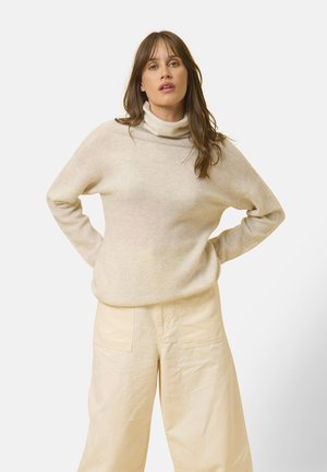 Beige kauluspaita, joka on valmistettu pehmeästä kankaasta, jossa on rento muotoilu ja pitkät hihat, yhdistetty vaaleisiin leveisiin housuihin.